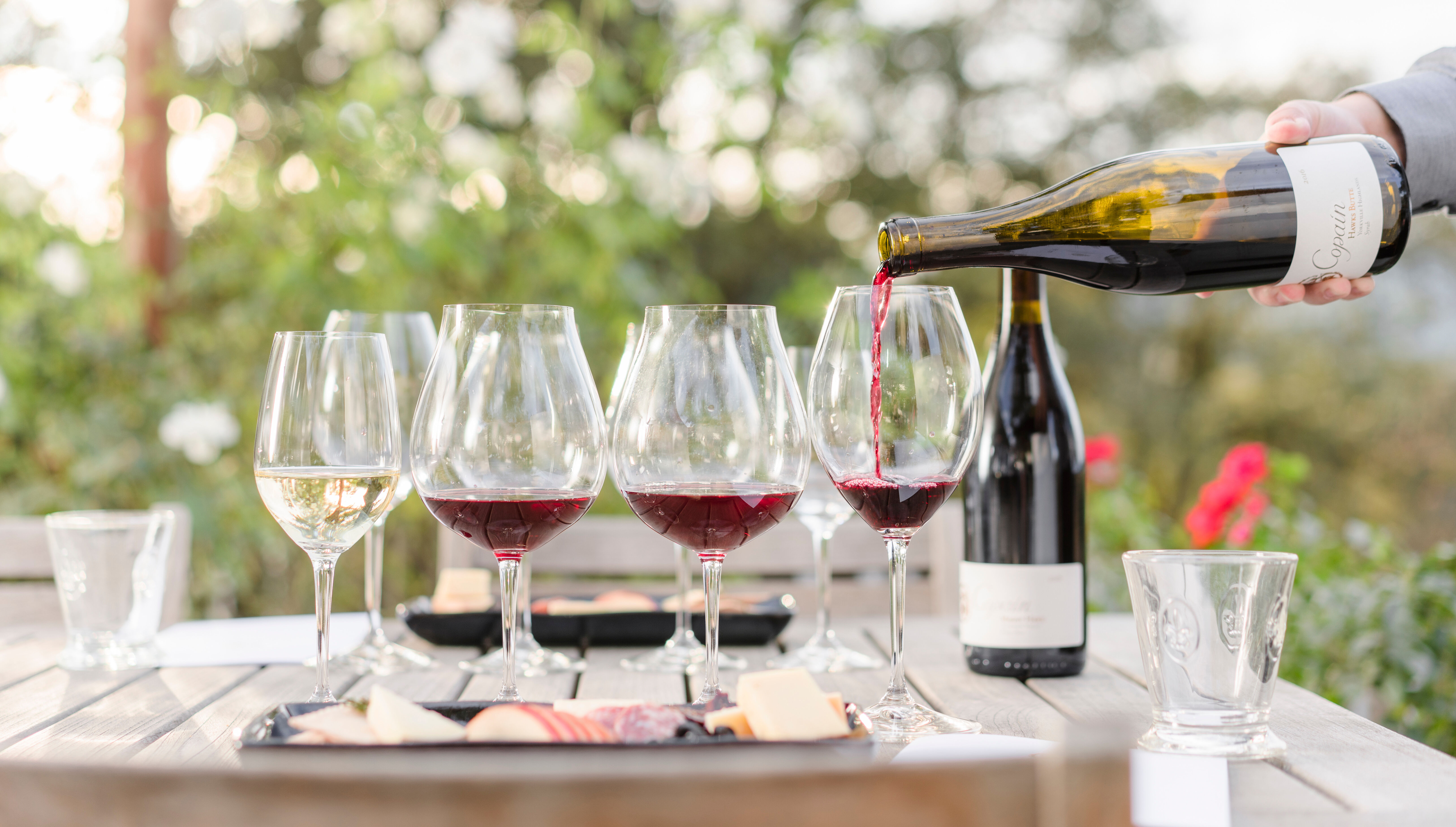A number of filled wine glasses, and one being filled from a wine bottle.